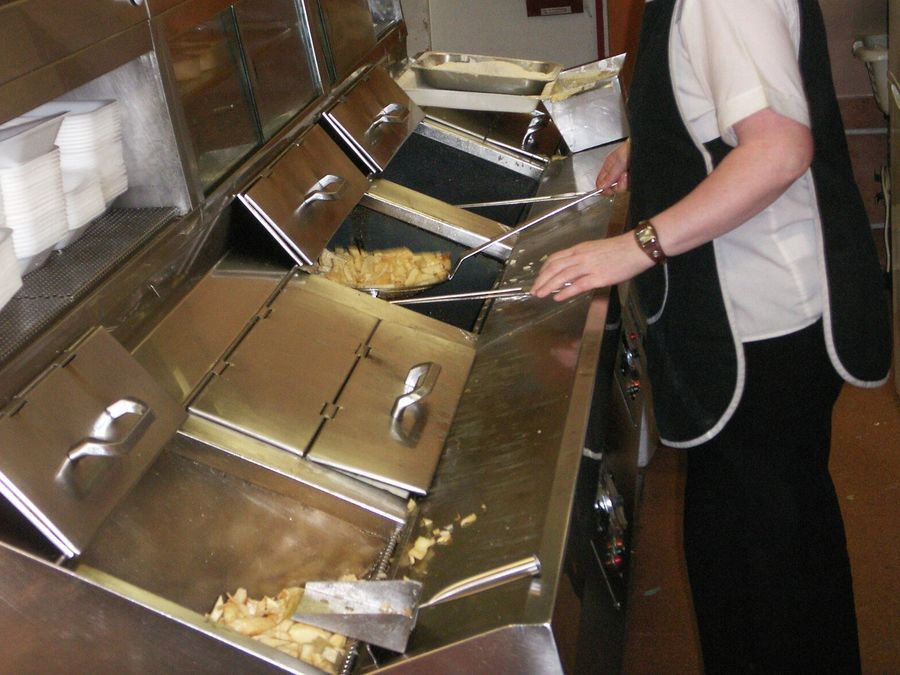 Hands lifting fries out of the oil with tongs at a stainless frying range