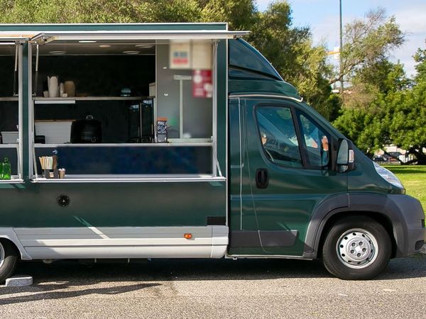A dark green food truck parked with its serving window open on a sunny day